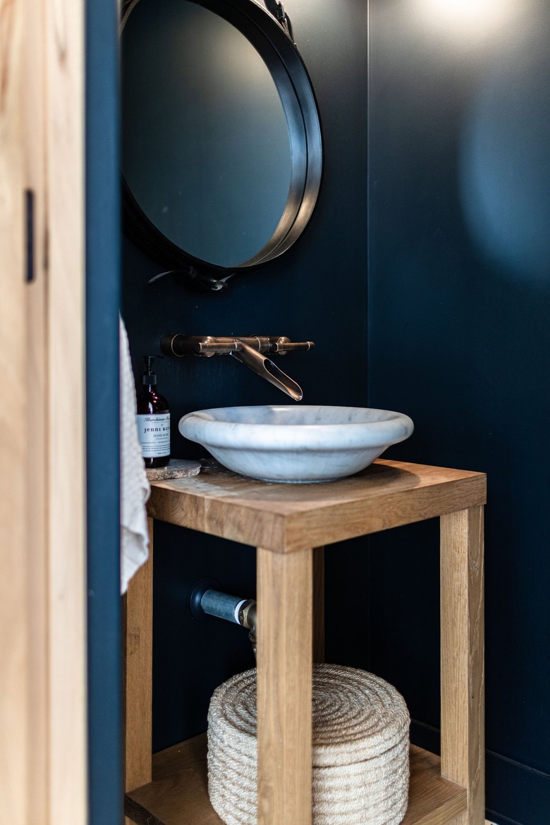 A blue walled bathroom with a white sink and wood vanity