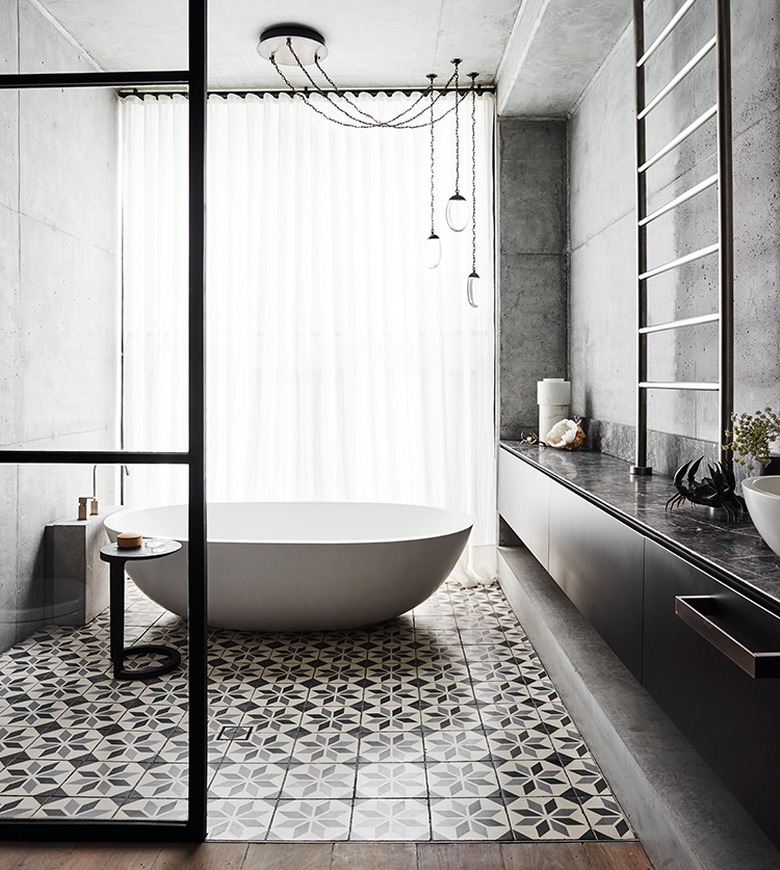 patterned bathroom tile idea on floor and freestanding tub with concrete walls and floor-to-ceiling window