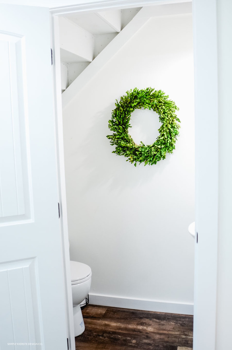 Bathroom under stairs with white walls and green boxwood wreath