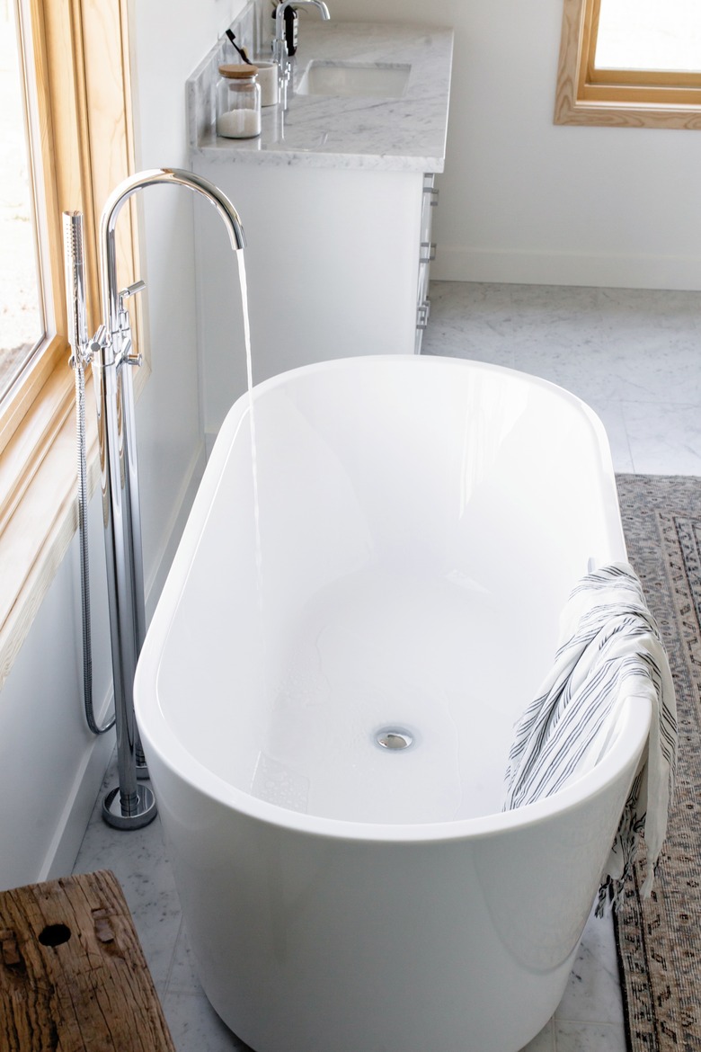 water filling up a freestanding white tub with a visible silver drain