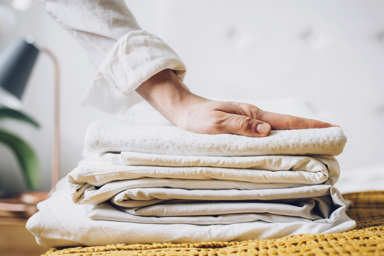 Folded bed sheets on top of mustard yellow blanket.