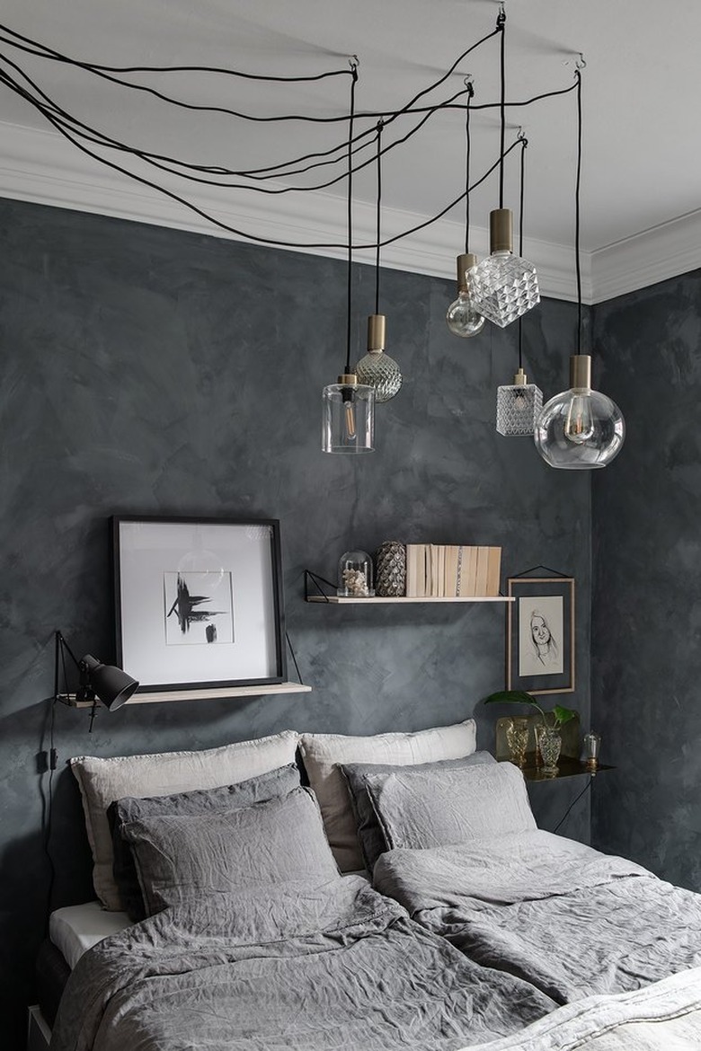 A gray vintage inspired bedroom with dark gray walls and lighter gray bedding and multiple hanging pendants