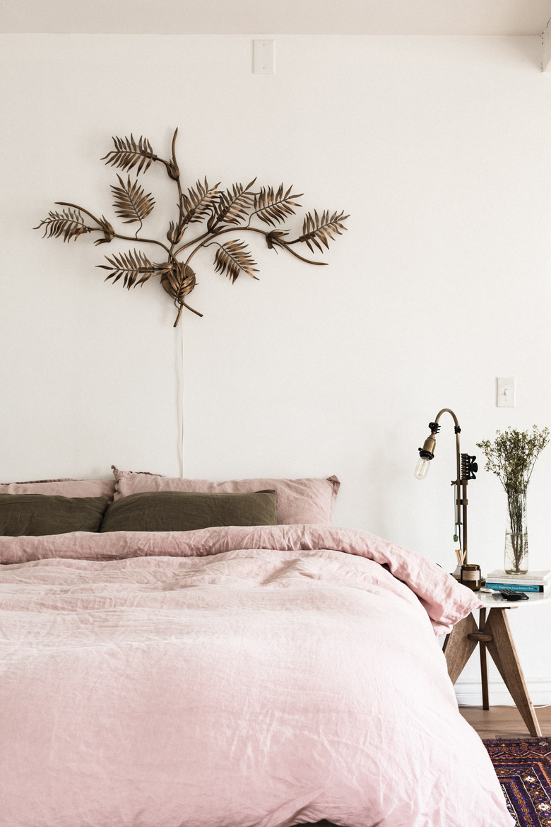 Bedroom with blush colored bedspread and brass artwork on wall