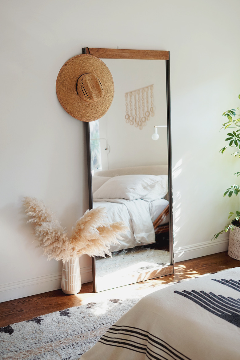 Standing bedroom mirror near bed with vase full of pampas grass sitting on floor