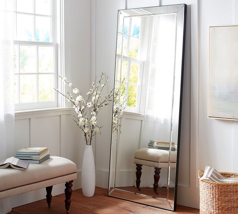 leaning frameless bedroom mirror next to accent bench and vase of flowers