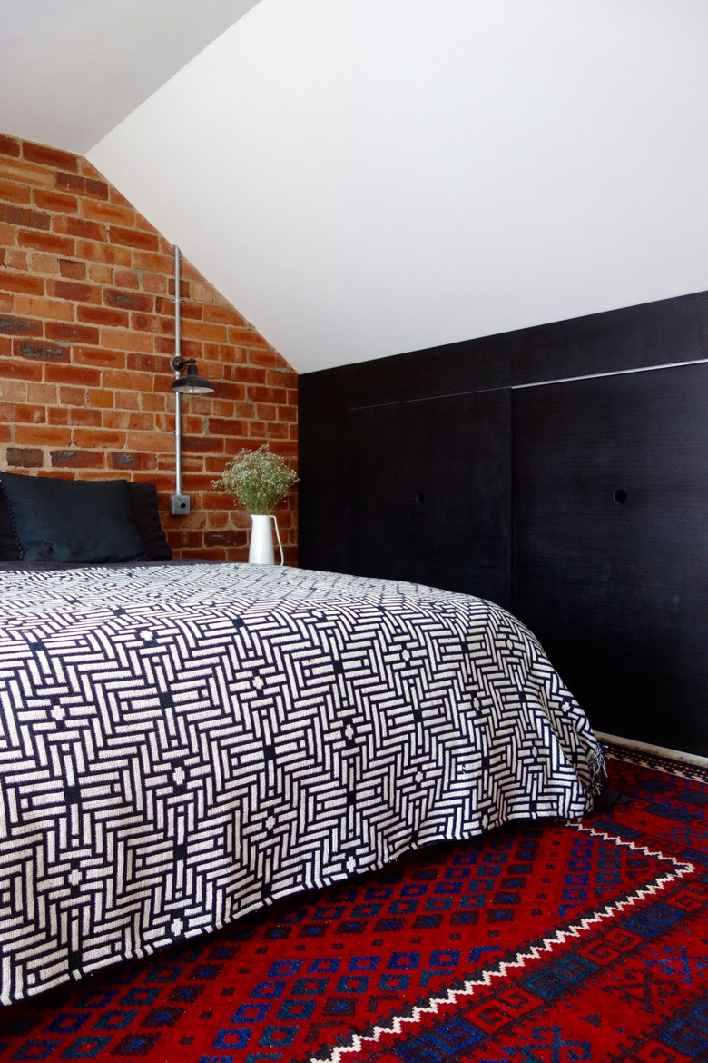 Industrial bedroom style with black accent wall and exposed brick with patterned bedding and rug