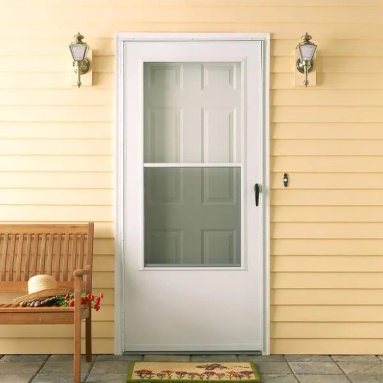 A white storm door on a house with yellow siding; a bench sits next to the door