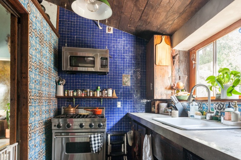 A kitchen with a wood ceiling, gray counter, and wood cabinets. Walls with blue tile and traditional geometric tile.