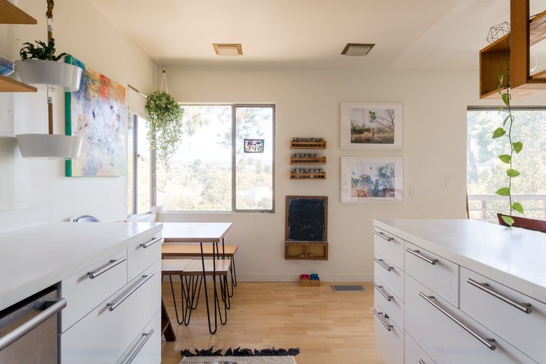 Kitchen with white cabinets, hairpin leg dining furniture, hanging plants, wood shelves, and wood floors.