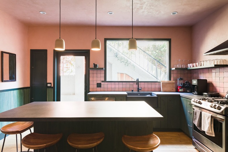 Kitchen with pink walls, green cabinets, gray counters, pink tile backsplash, bell pendant lights and wood floor.