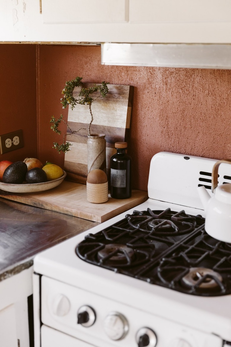 Kitchen corner with a small stove, dish of fruit, wood cutting boards, and vase with a plant clipping.