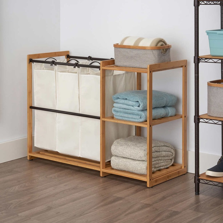 Costco's bamboo laundry station organizer, consisting of three white hampers, and two shelves to the side. There are towels resting on each shelf.