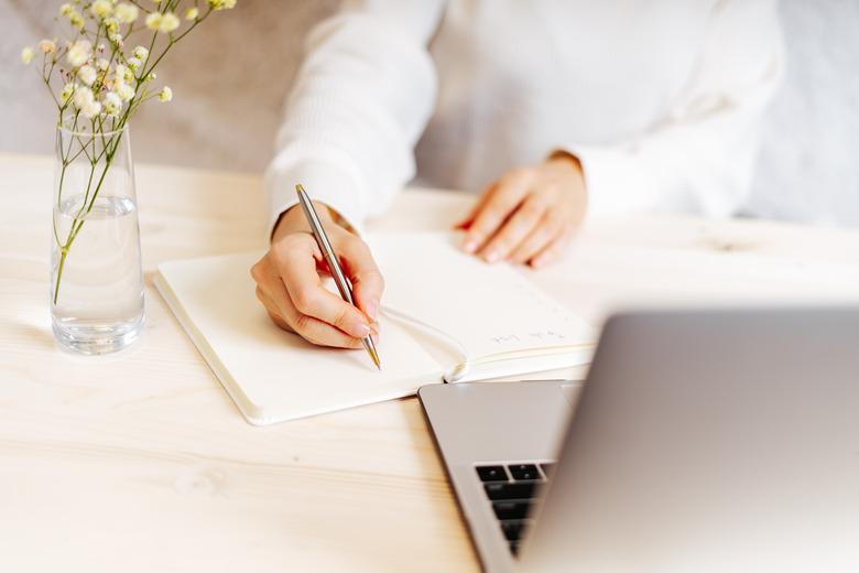 Woman writes in notebook on desk with laptop