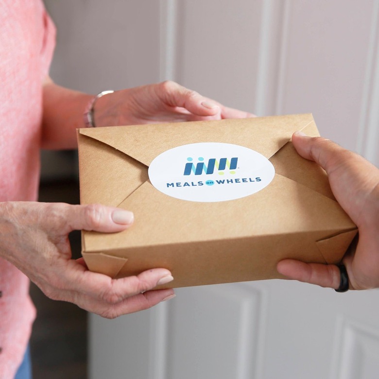 Hands giving another hand a to-go food box that reads 