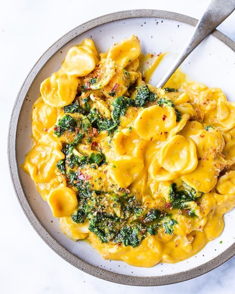 A white plate of orecchiette pasta covered in orange carrot miso sauce and topped with toasted bread crumbs.