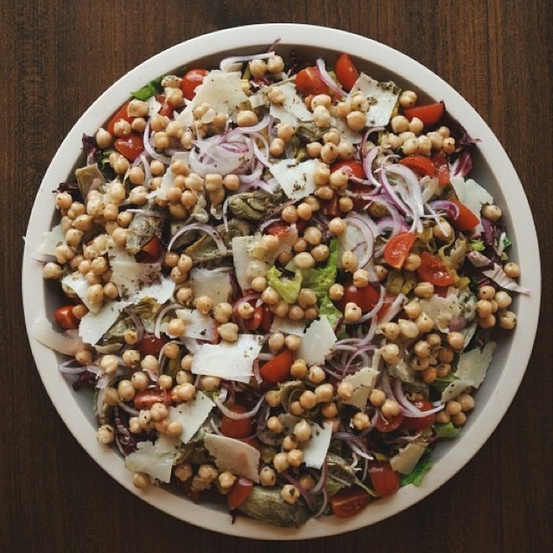 A vegetarian chopped antipasto salad featuring onions, chickpeas, tomatoes, and artichokes on a large white plate.