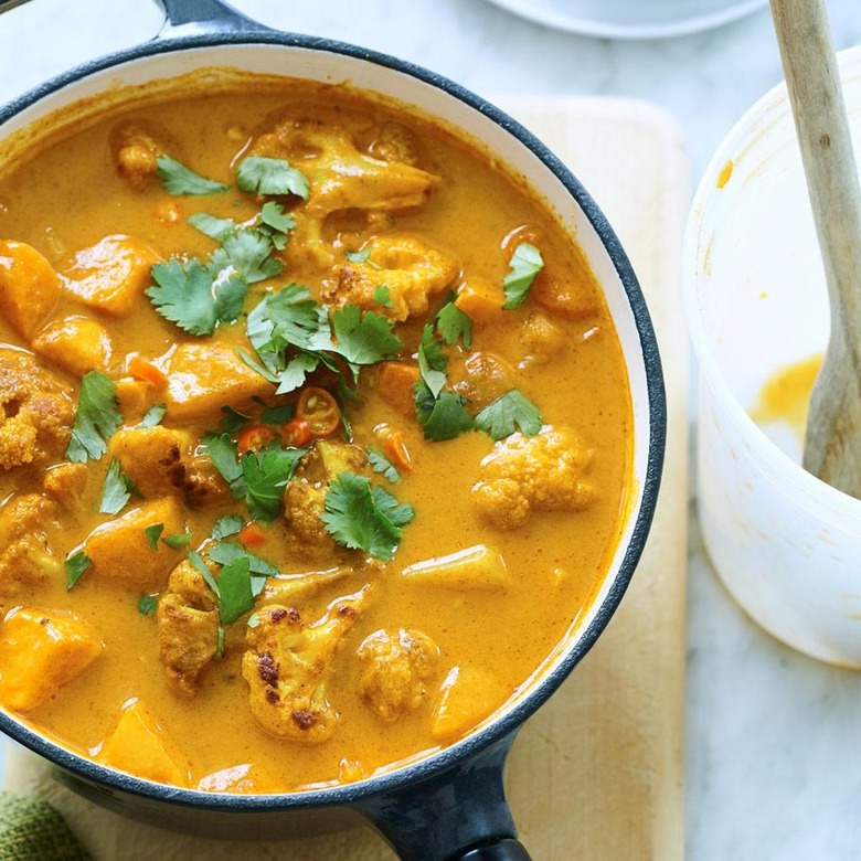 A roasted cauliflower and potato curry soup in a white bowl lined with blue around the rim.