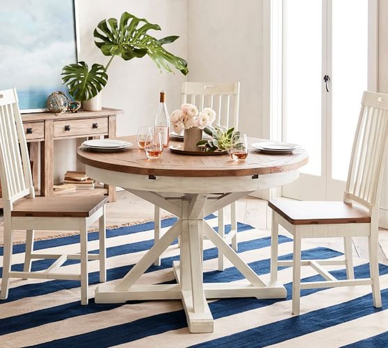 Image of round dining table with three chairs around it. The table is distresses white with a brown tabletop. There are flowers, wine and plates on the table.