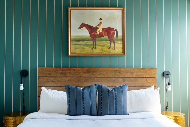 Eclectic bedroom with rustic wood headboard, painting, green striped wallpaper, black sconces