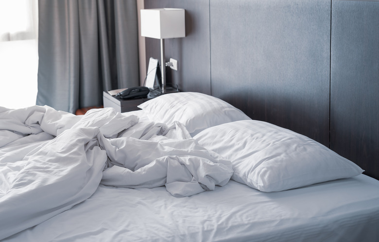 Messy and unmade white hotel bed at hotel room in holiday morning.