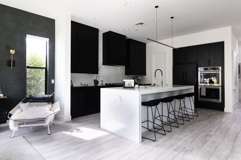 Modern kitchen with black cabinets, gray wood floors and white counters