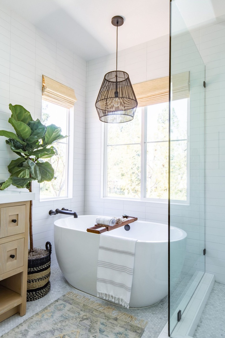 white modern bathroom with freestanding tub and black tub fixtures, woven lamp hanging above and next to it, a glass shower door