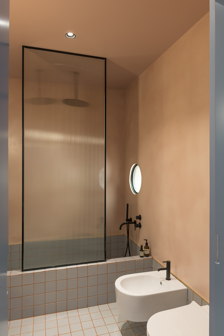 terra cotta minimalist bathroom with glass shower door and blue-gray tile tub and black shower fixtures