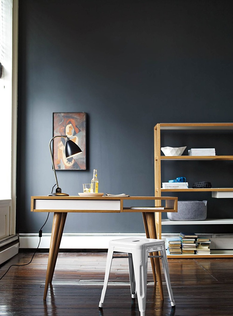 black home office with midcentury modern wooden furniture and large shelving unit in the back