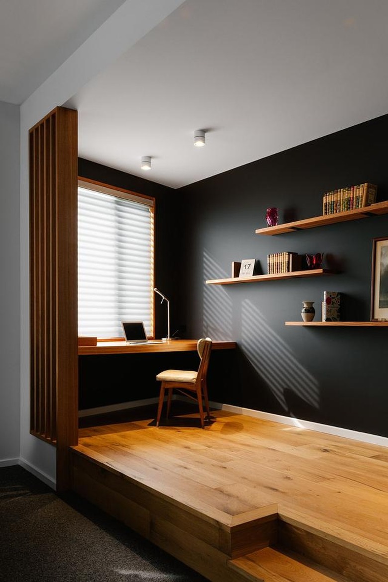 black and white home office with warm wood flooring and a desk sitting underneath a window