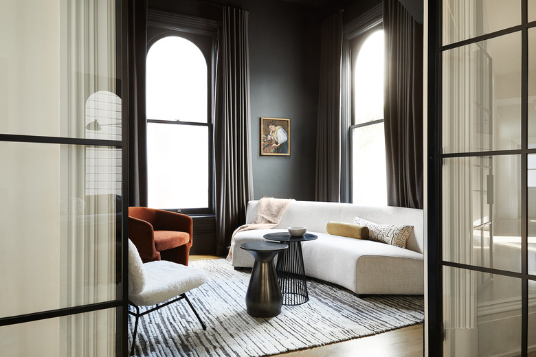 black windows in living room with burnt orange chair and white couch