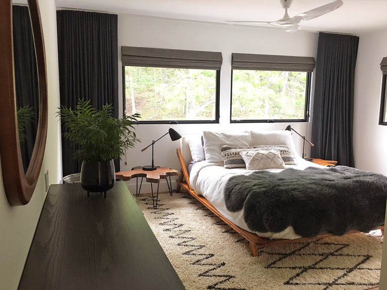 black windows in bedroom with geometric pattern rug, platform bed, and tree stump bedside table