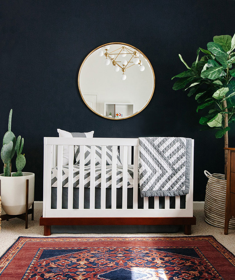 Navy blue nursery idea with white crib and round mirror hanging above with potted plants