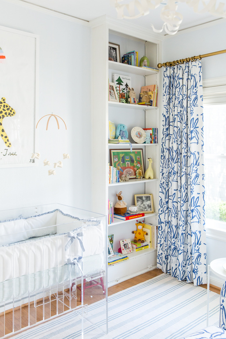 Blue nursery idea with patterned drapery at window and built-in bookcase filled with books and toys