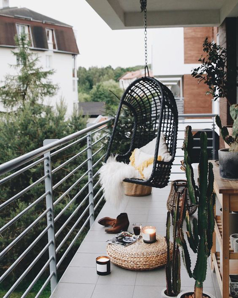 bohemian balcony idea with black hanging chair and woven floor pouf