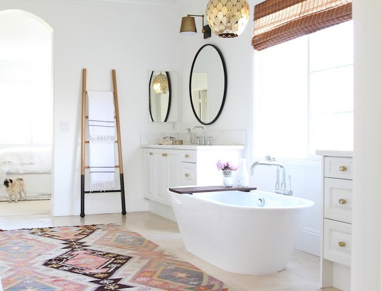 white bathroom with freestanding tub and patterned rug with towel ladder