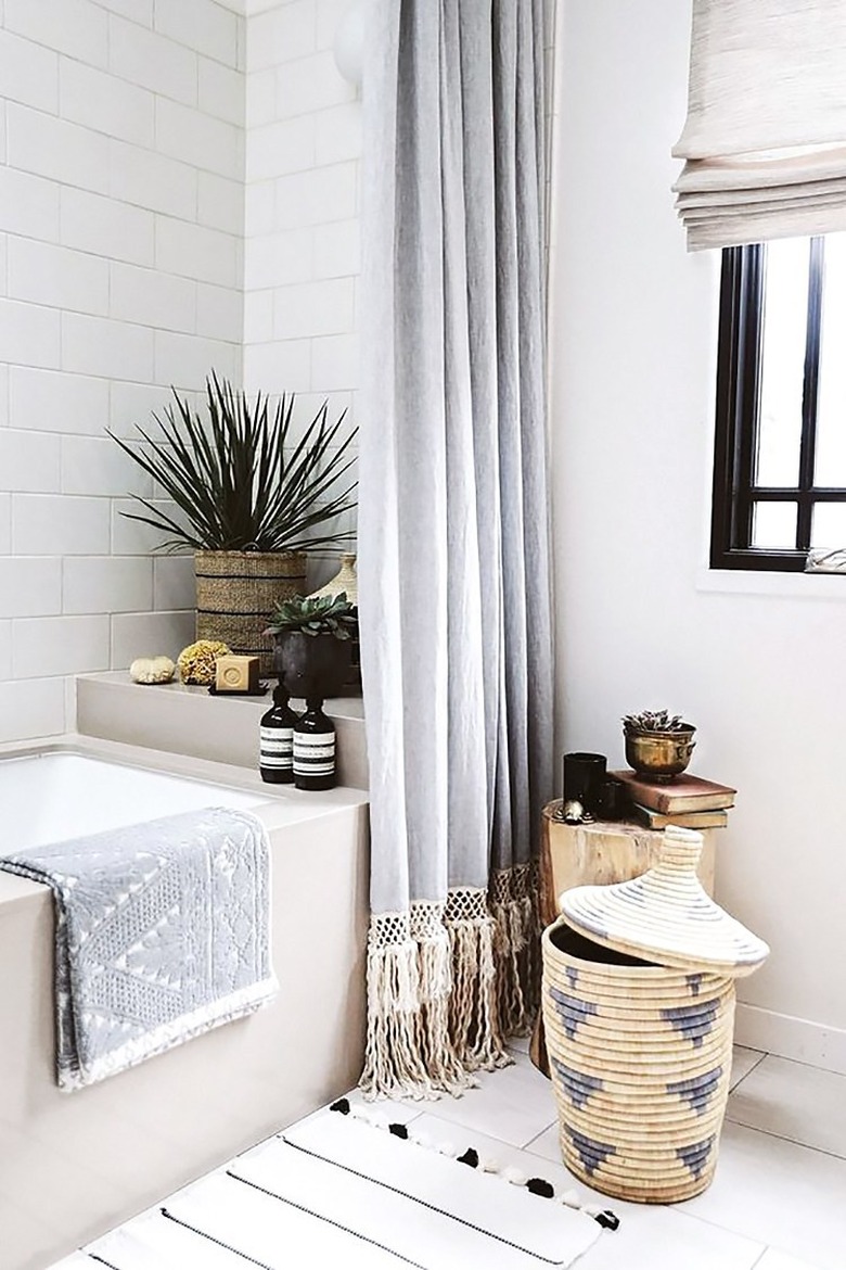 white bohemian bathroom idea with woven baskets and potted plants with Roman shade at window