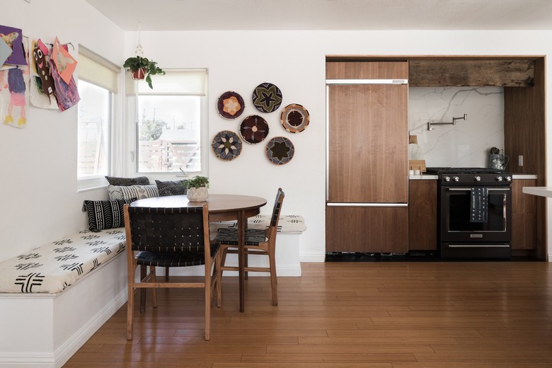 Kitchen with wood cabinets, wood-lattice chairs, banquette bench, geometric cushions, and colorful basket decor.