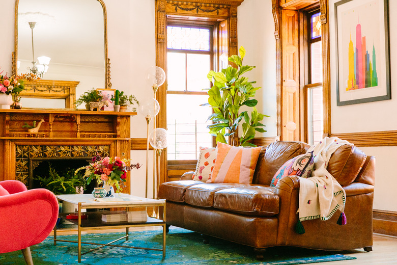 Boho apartment decor in living room with leather couch, wood fireplace, and midcentury floor lamp