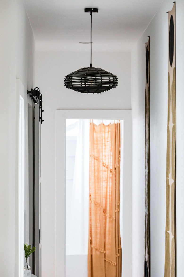 A black abstract pendant light in a white-walled hallway and an orange curtain