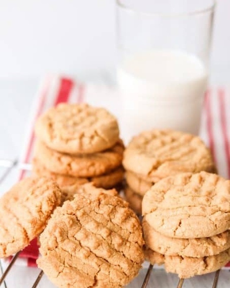 Stacks of peanut butter cookies next to a glass of milk on a red and white striped towel.