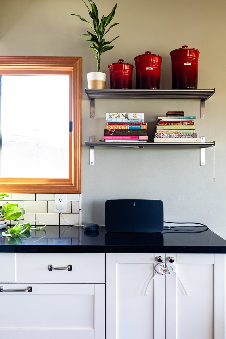 A kitchen with black countertops, white cabinets and metal shelving