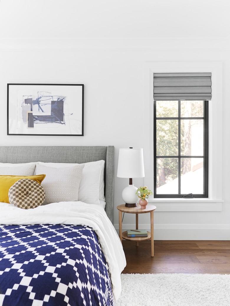 Bedroom with mustard yellow accent pillow and upholstered gray headboard and wooden side table