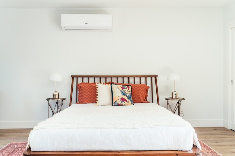 A bed with a wood dowel headboard, white bedding, multi-colored pillows, and symmetrical nightstands and lamps