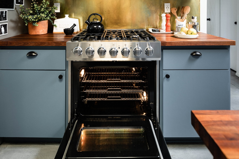 open stainless steel oven surrounded by light blue cabinets and wood countertops