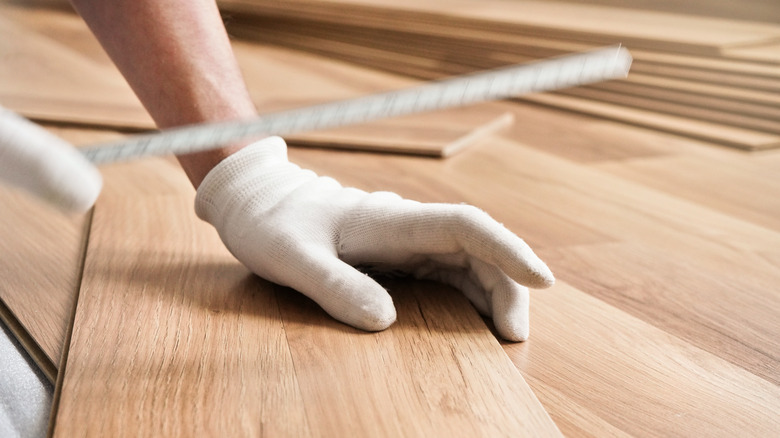 Installing laminated floor, detail on man hands in white gloves, holding measuring tape over wooden tiles