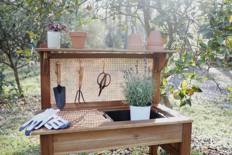 Potting bench with cane webbing stapled to back and garden tools hanging from cane webbing