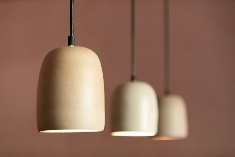 A trio beige bell pendant lights with black cords.