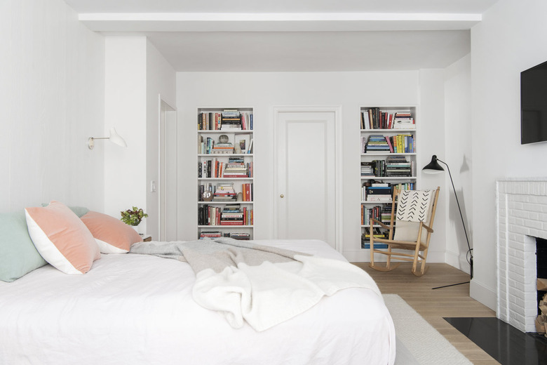 celadon colors on bed pillows in white bedroom with fireplace