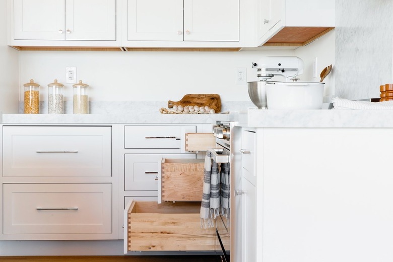 In a kitchen, white drawers with a marble countertop and white cabinets above. Three of the drawers are open to varying degrees. On the countertop, there's a white KitchenAid stand mixer, three glass storage containers, and a white pot.