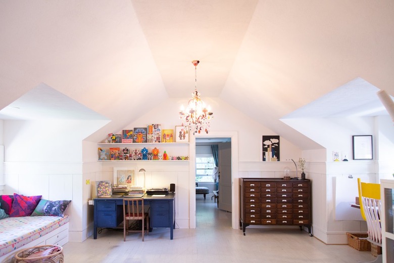 An attic with a chandelier, built-in white bookshelves, and colorful accents.